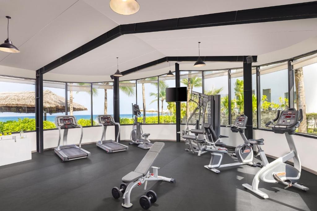 A bright glass-walled fitness room overlooking palm trees and the sea.