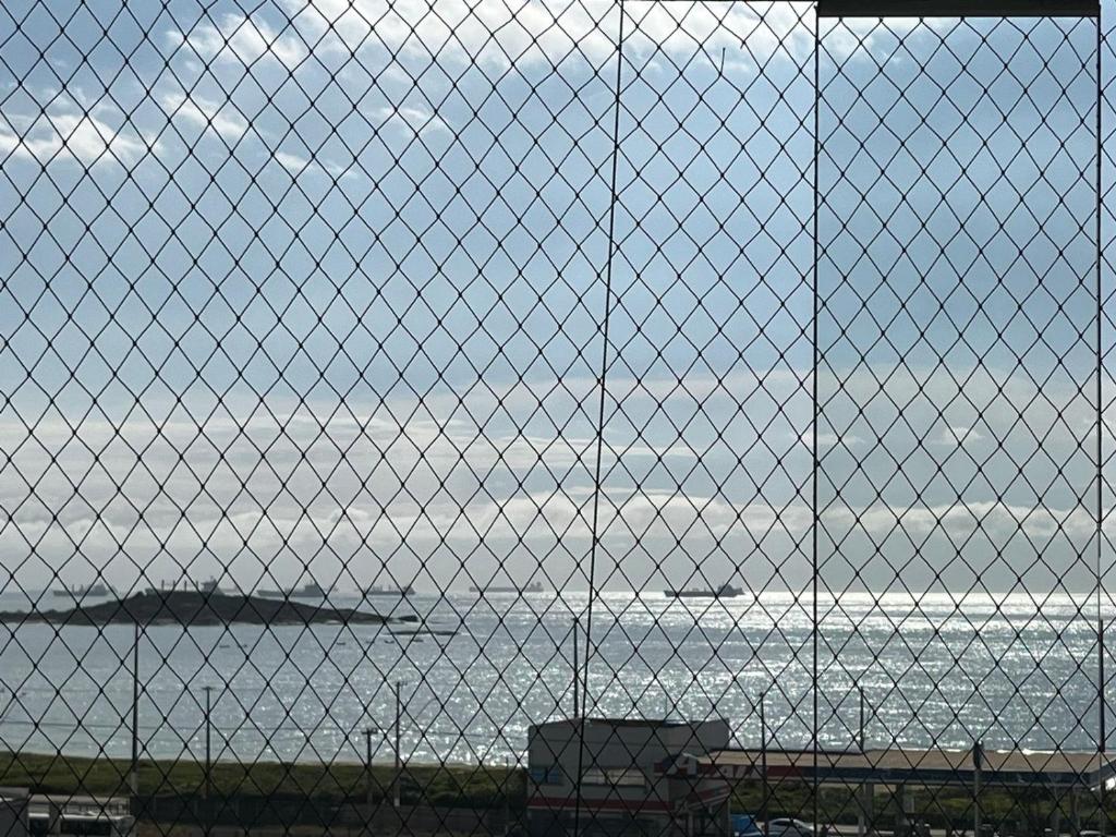 a view of the ocean through a chain link fence at Praia de Itaparica com Vista para o Mar in Vila Velha