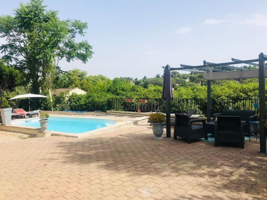 une terrasse avec une piscine, des chaises et un parasol dans l'établissement Maison au calme proche ville, à Nîmes