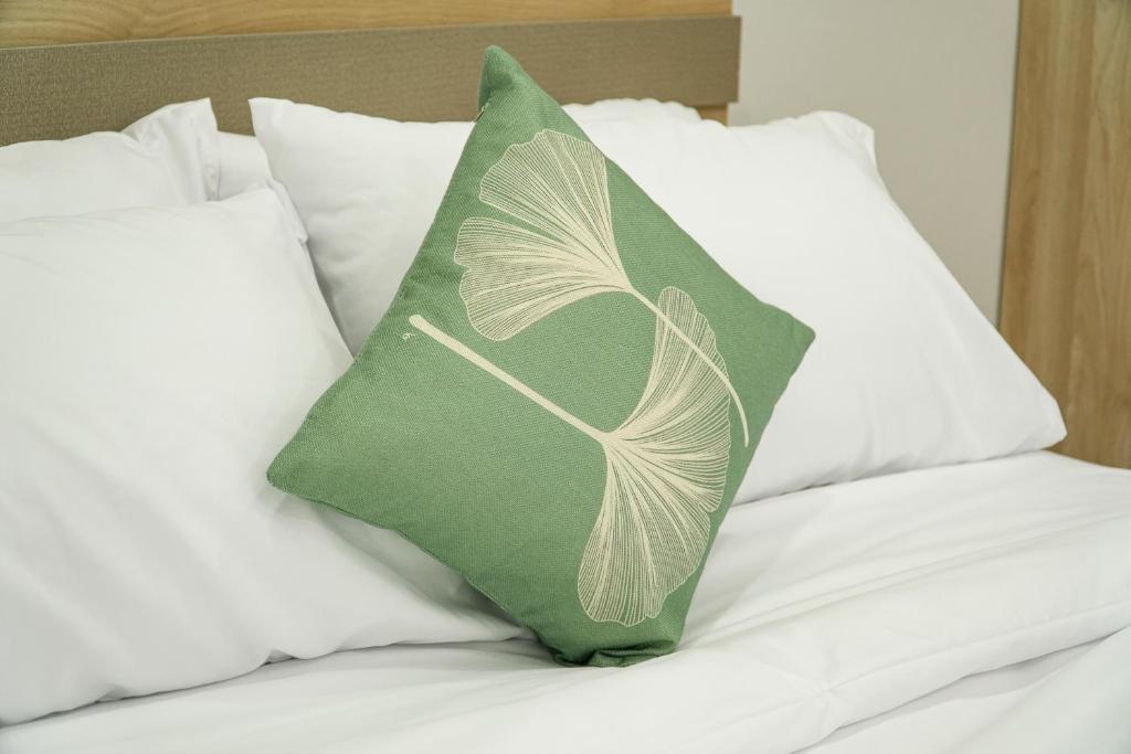 almohada verde en una cama con almohadas blancas en เมตตา เรสซิเด้นซ์ - Metta Residence, en Ban Dam Phra