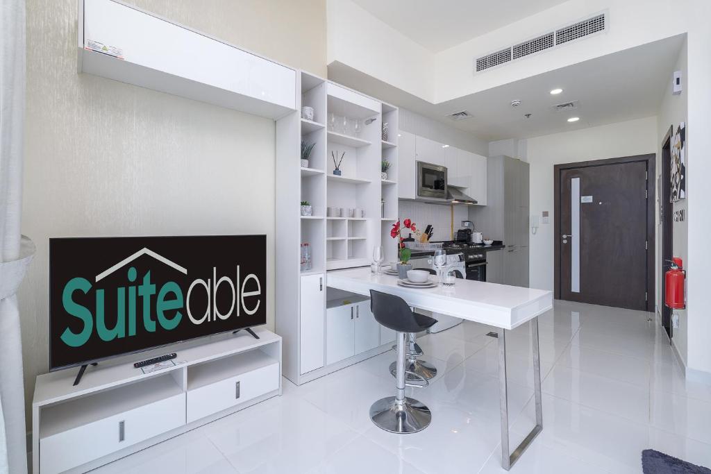 eine weiße Küche mit einem Tisch und einem TV in der Unterkunft Placid Studio close to Dubai Miracle Garden in Dubai