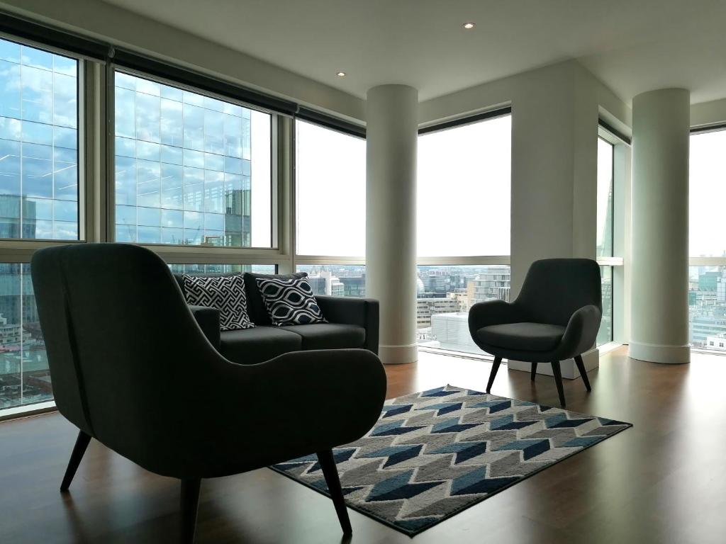 uma sala de estar com um sofá, cadeiras e janelas em Still Life Aldgate Deluxe em Londres