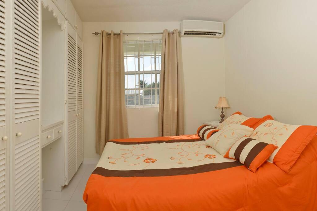 an orange bed in a white room with a window at Sunset Nook: Cozy one bedroom apartment in Saint James