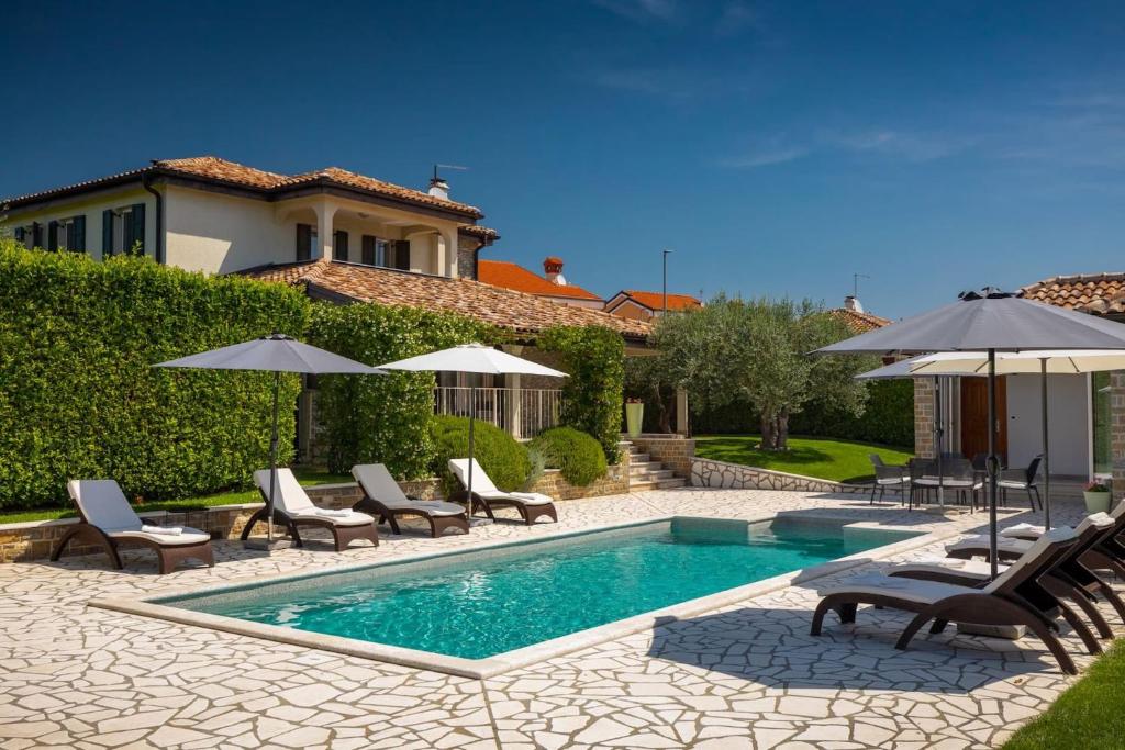 a swimming pool with chairs and umbrellas next to a house at Rustic villa Inga with pool and grill in Buje in Kaštel