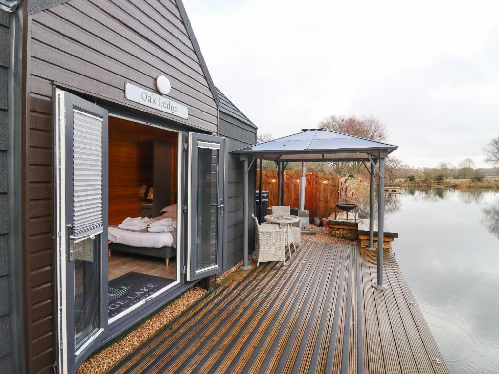 ein Haus mit einer Terrasse neben dem Wasser in der Unterkunft Oak Lodge At Bridge Lake Farm & Fishery in Banbury