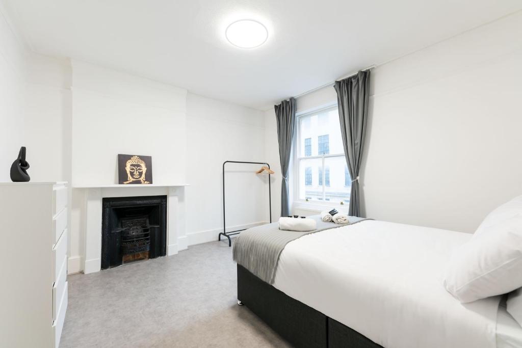 a white bedroom with a bed and a fireplace at Luxury 2 Bedroom Flat in Balcombe Street in London