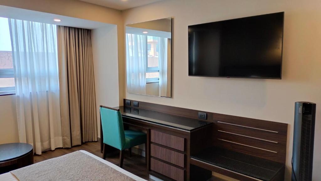 A compact in-room work area with a desk, chair, television, and curtained window.