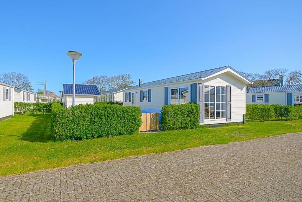 ein blau-weißes Haus mit Hecke in der Unterkunft Chalet Luttikduin 22, met ruime tuin! - Callantsoog in Callantsoog