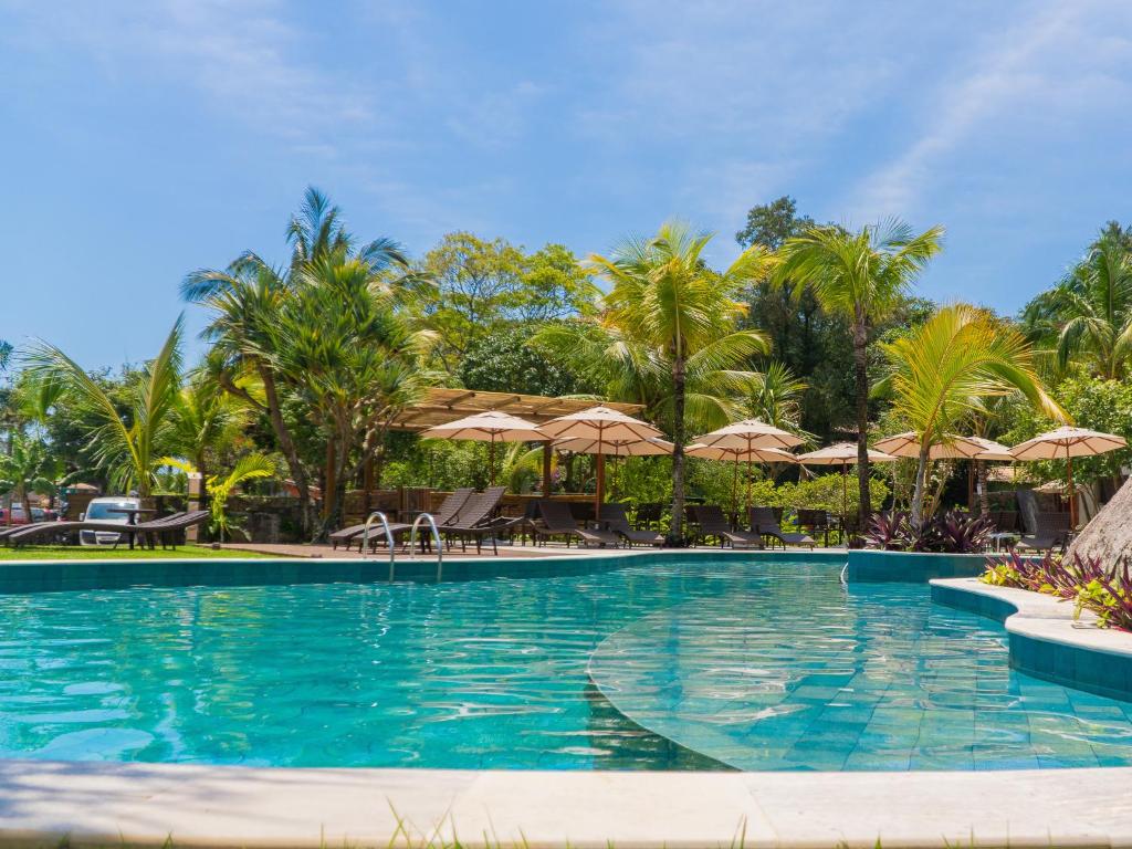 a swimming pool with palm trees and umbrellas at Velas do Engenho in Ilhabela
