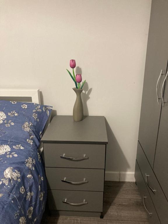 een vaas met bloemen op een nachtkastje naast een bed bij Kingdom Holiday - 12 Hamilton in Londen