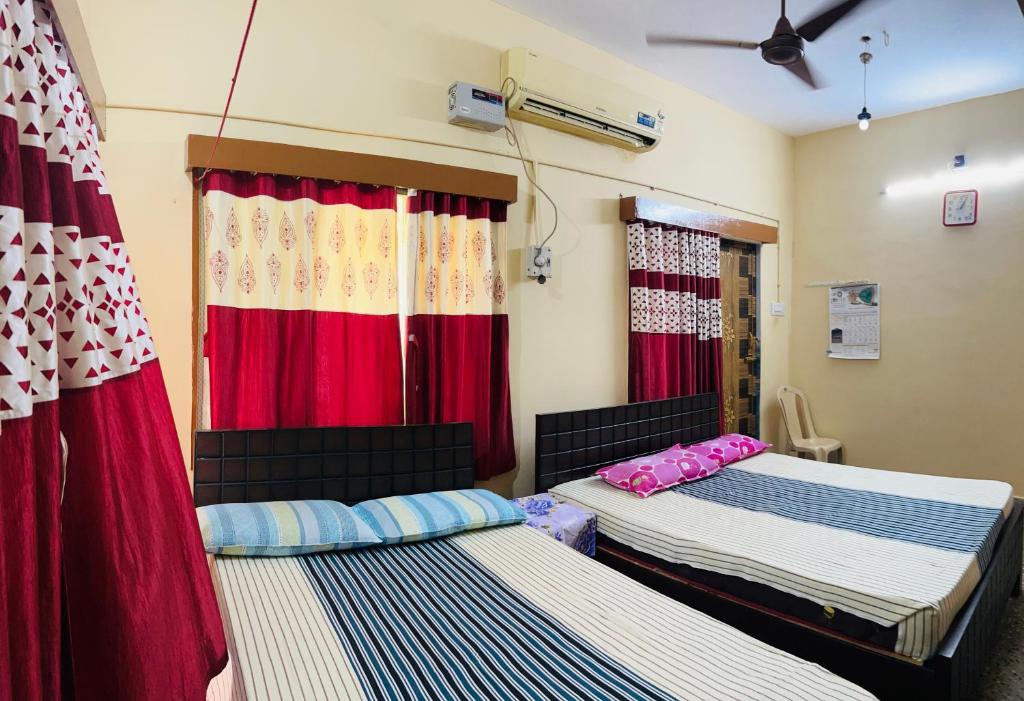 two beds in a room with red curtains at Sirvachur madhurakalli amman guest house in Perambalūr