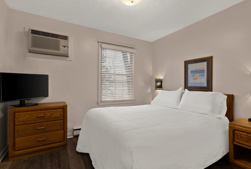 um quarto com uma cama branca e uma televisão de ecrã plano em Traverse Bay Inn em Traverse City