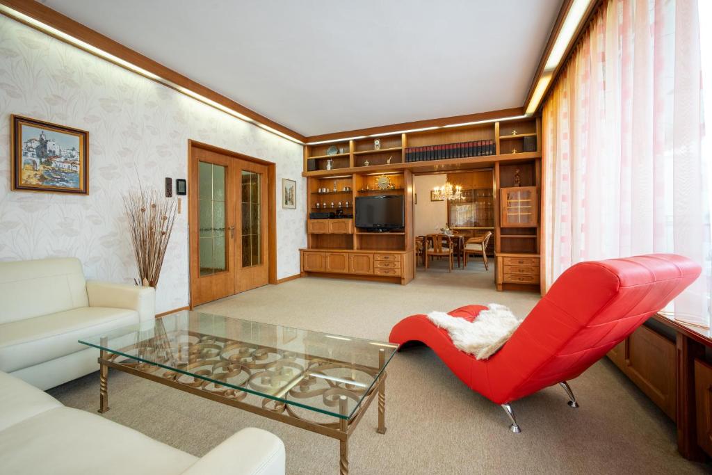 Innsbruck Garden Residence في إنسبروك: غرفة معيشة بها كرسي احمر وطاولة زجاجية