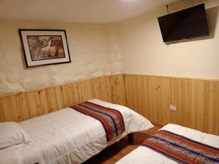a bedroom with two beds and a flat screen tv at Paucartambo wasichay hostal in Cusco