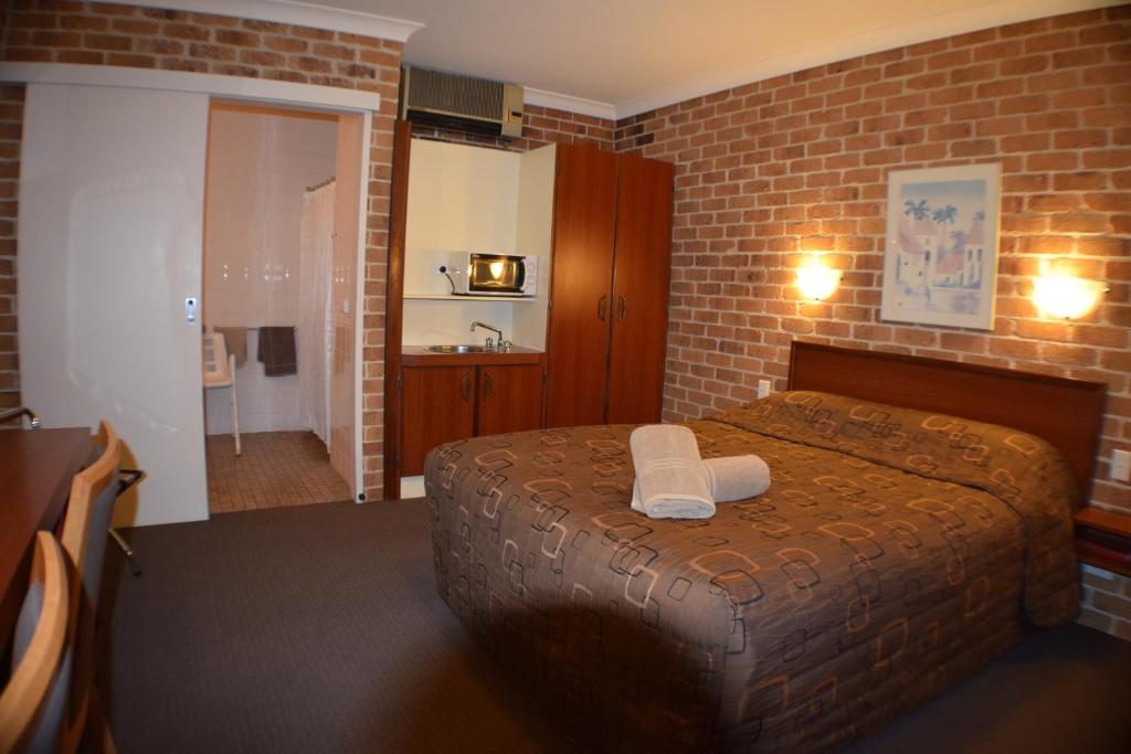 a bedroom with a bed and a brick wall at Acacia Motor Inn in Armidale