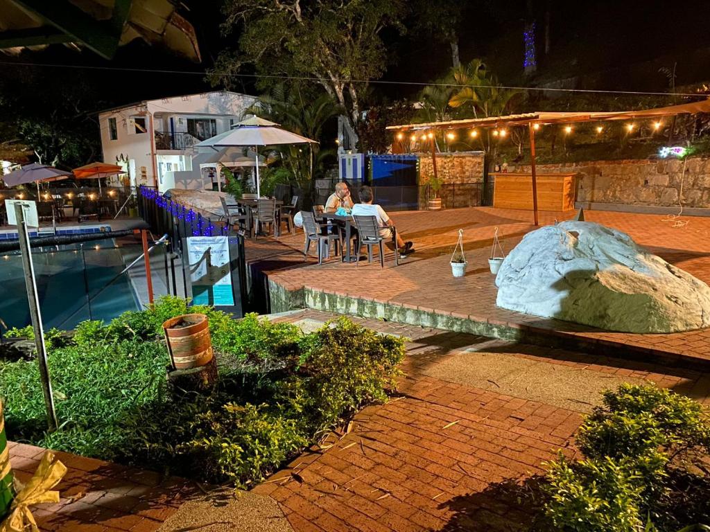 una mujer sentada en una mesa junto a una piscina por la noche en Eco Hotel Entre Ríos, en Villeta