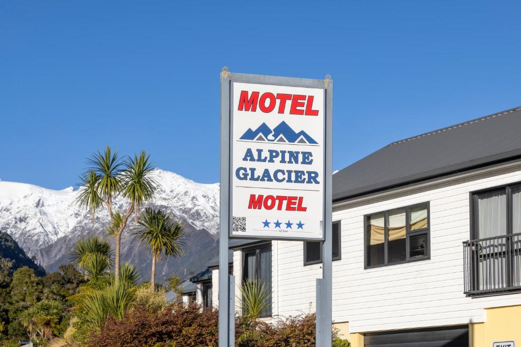 a motel sign in front of a building with mountains at Alpine Glacier Motel in Franz Josef