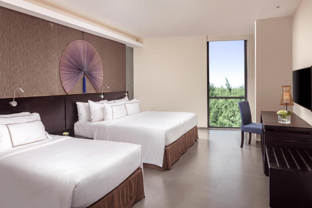 A simpler twin room with a narrow desk, two beds, a window and a dark wood television console.