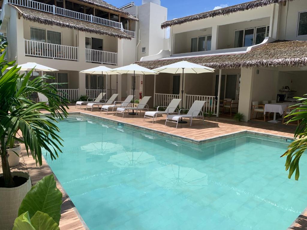 a swimming pool in front of a hotel with chairs and umbrellas at Le Clos des Bains Mauritius in Blue Bay