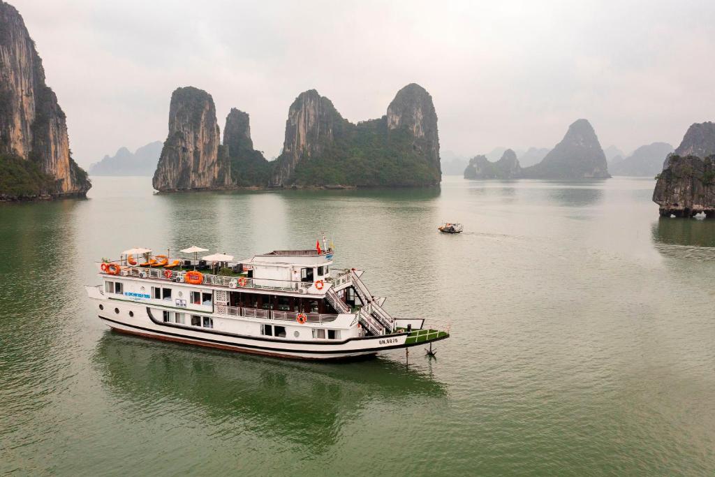 um barco na água com montanhas ao fundo em Ha Long Fantasea Legend Cruise em Ha Long
