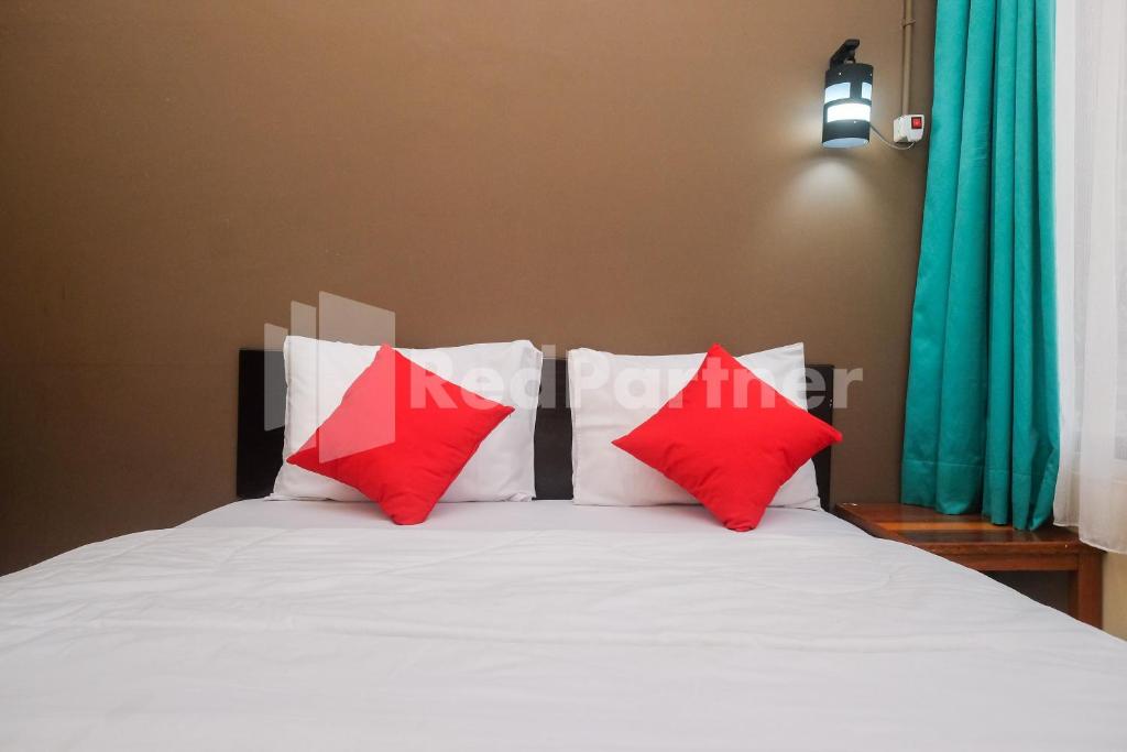 um quarto com uma cama branca e almofadas vermelhas em Travelista Homestay near GOR Candradimuka Semarang Mitra RedDoorz em Srondolwetan