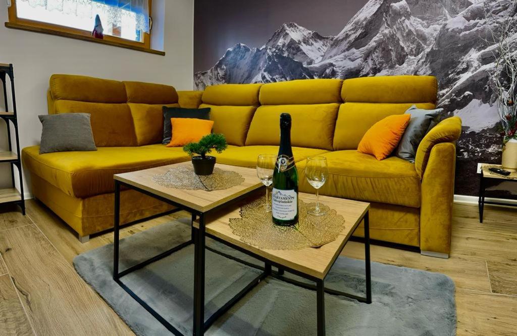 a yellow couch with a bottle of wine and two tables at Apartament Szafran ApartamentyZakopianskie Basen Sauna Jacuzzi in Zakopane