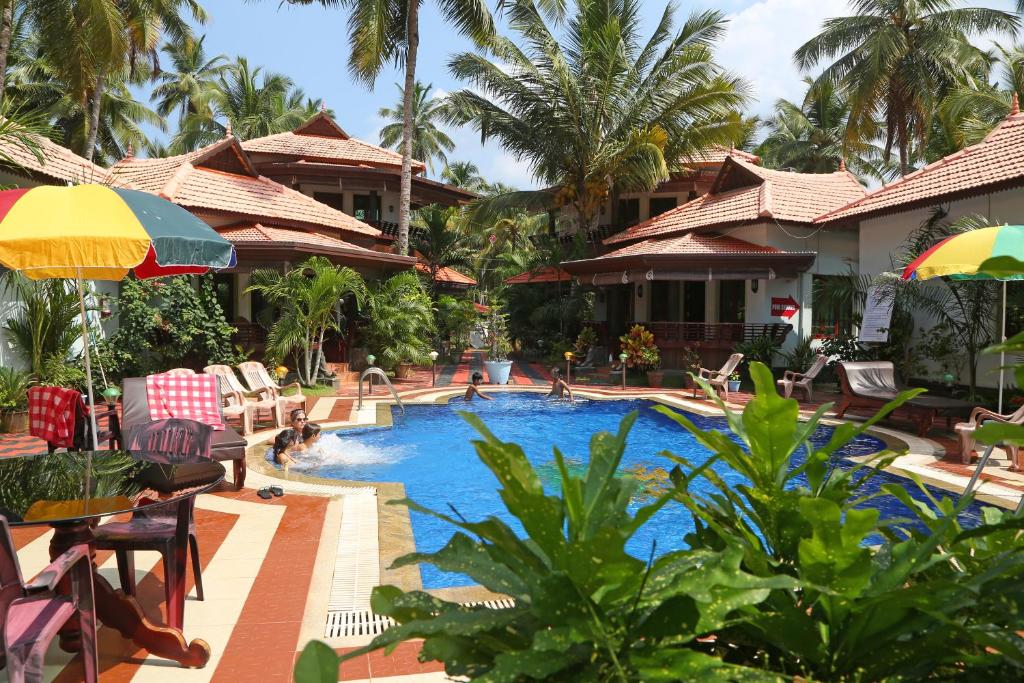 a resort pool with tables and chairs and palm trees at Samsara Harmony Beach Resort in Varkala