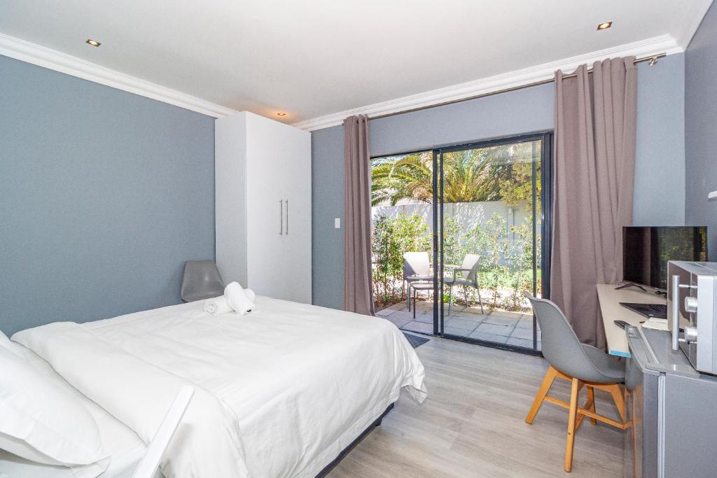 a bedroom with a bed and a desk and a balcony at Bloubergstrandlodge in Bloubergstrand