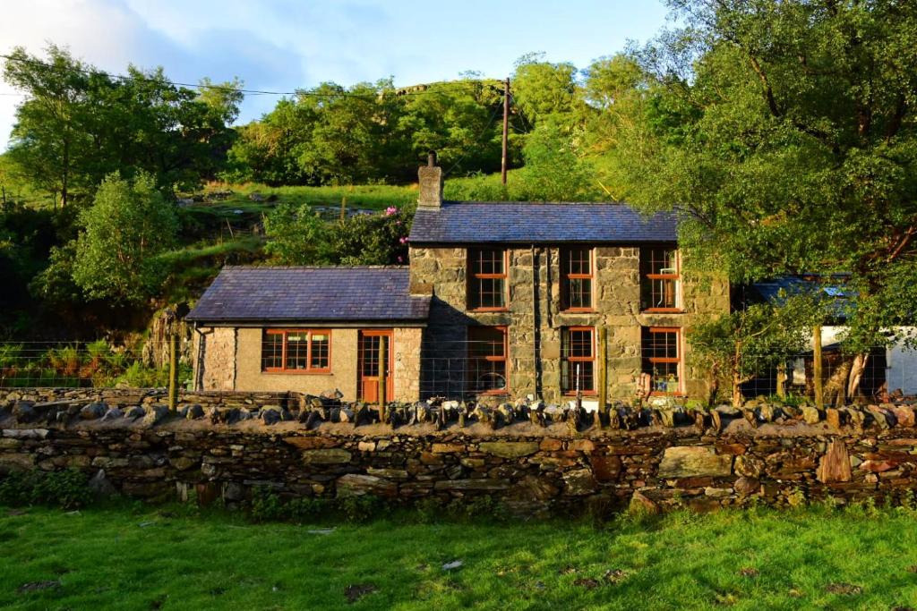 a stone house sitting behind a stone wall at Terfyn Cottage in Dinorwic
