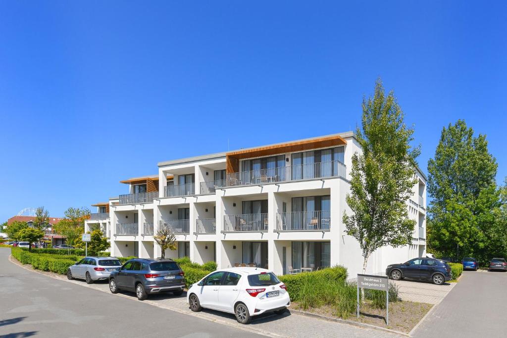 Un edificio blanco con coches aparcados delante. en Ferienwohnung 1-24 im Deichhaus 1, en Wohlendorf
