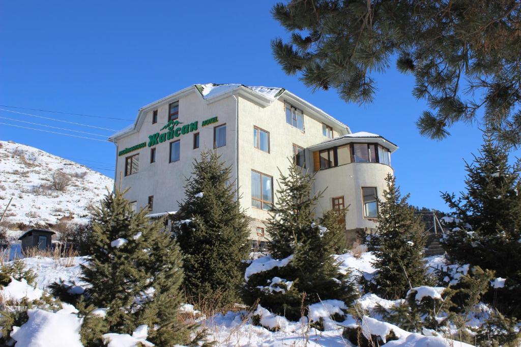 a building in the snow with trees in front of it at Жайсан in Karakol