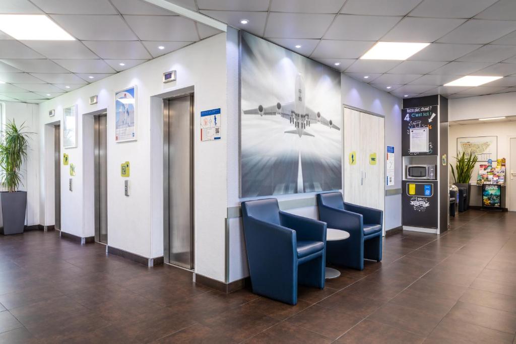 une salle d'attente avec des chaises bleues et un grand mur dans l'établissement ibis budget Roissy CDG Paris Nord 2, à Roissy-en-France