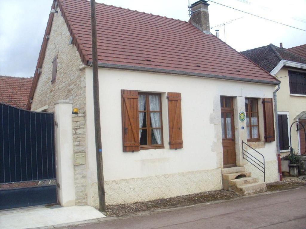 a small white house with wooden doors on a street at Le village in Polisy