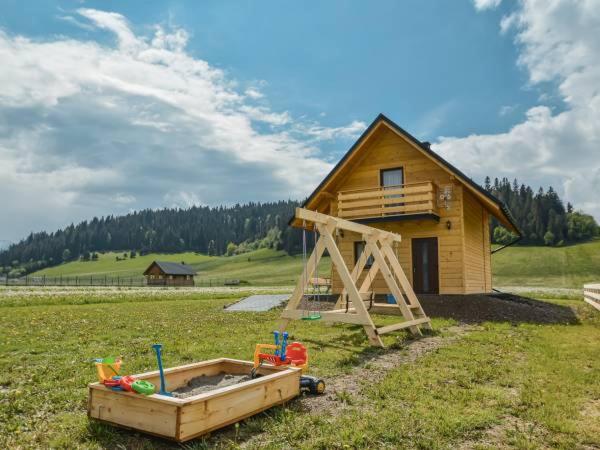 une petite maison en bois avec un bac à sable dans un champ dans l'établissement Spiska Chatka, à Kacwin