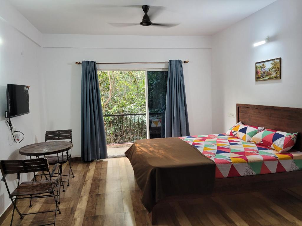 a bedroom with a bed and a table and a window at Miranda Guest House by Rosh Hospitality in Baga