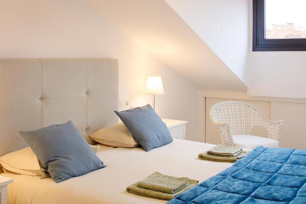 Un dormitorio con una cama con almohadas azules y una silla en Ático con terraza en playa de San Lorenzo, en Gijón
