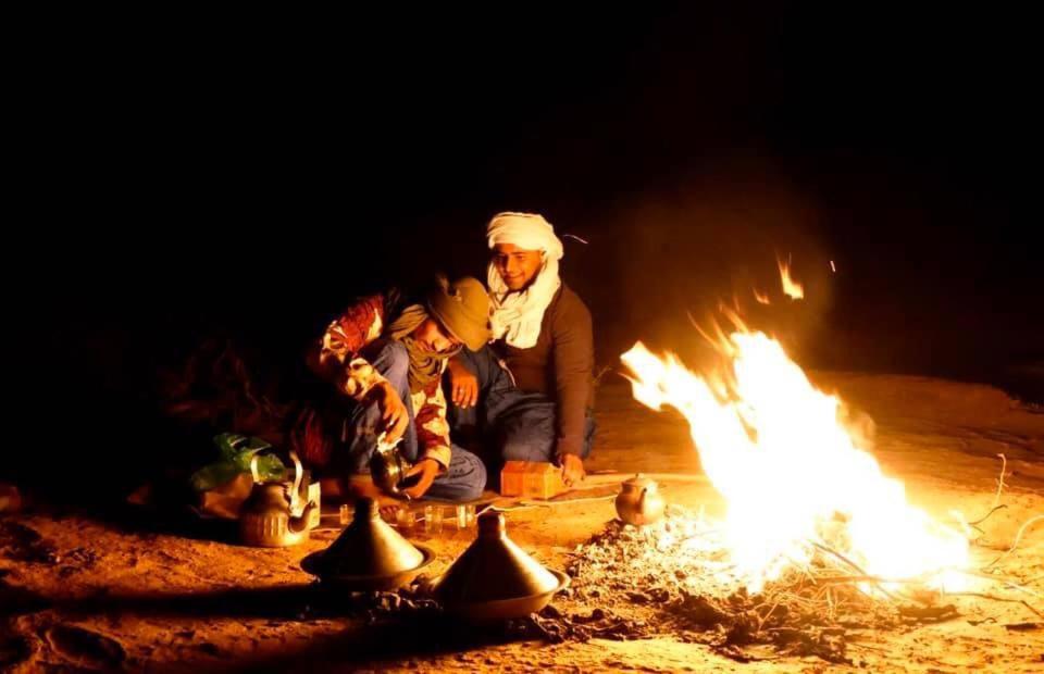 un hombre sentado junto al fuego por la noche en Mhamid yaya camp, en Mhamid