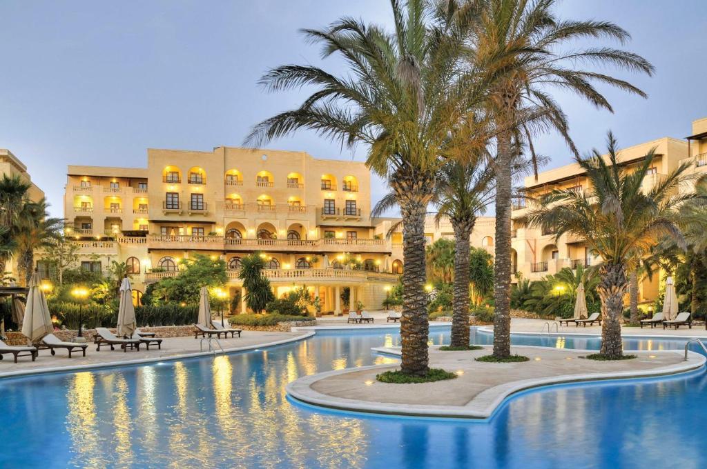 a hotel with palm trees in front of a pool at Kempinski Hotel San Lawrenz in San Lawrenz
