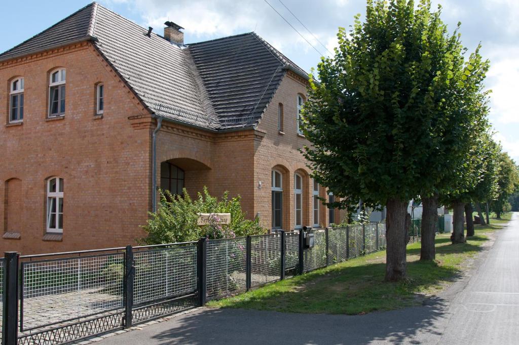 a brick house with a fence next to a tree at Ferienwohnung Alte Schule in Vetschau