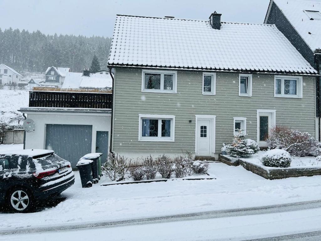 a house with a car parked in a yard covered in snow at Ferienhaus Sauerland - Traum in Winterberg