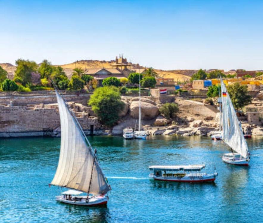 três veleiros num rio com uma cidade ao fundo em جوله بفلوكه في نهر النيل em Aswan