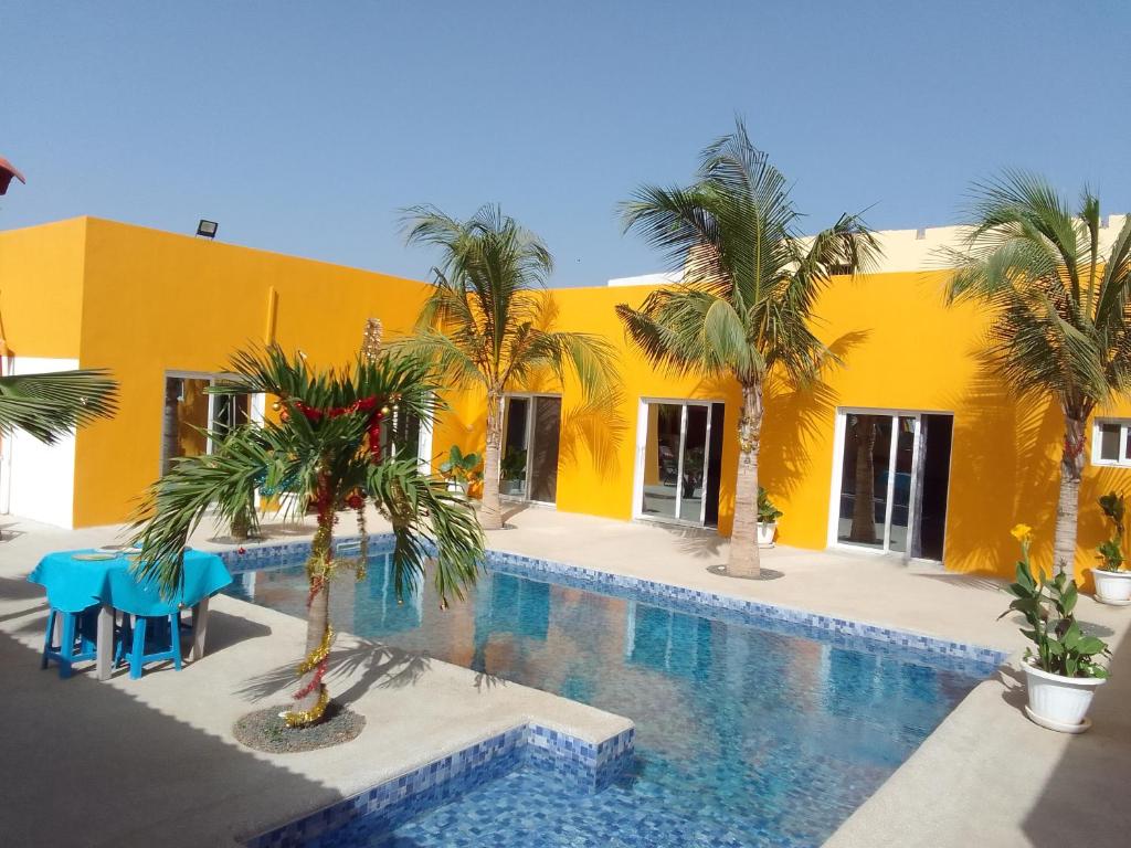 ein gelbes Gebäude mit einem Pool und Palmen in der Unterkunft Hôtel Colibri in Niaga
