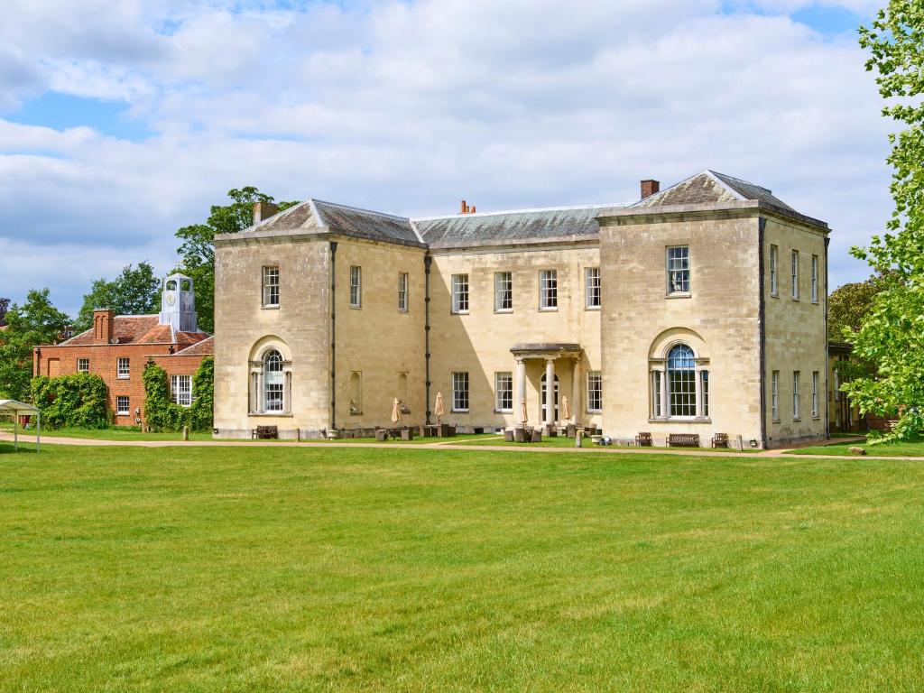 a large stone building with a large grass field at Hitchin Priory Hotel in Hitchin