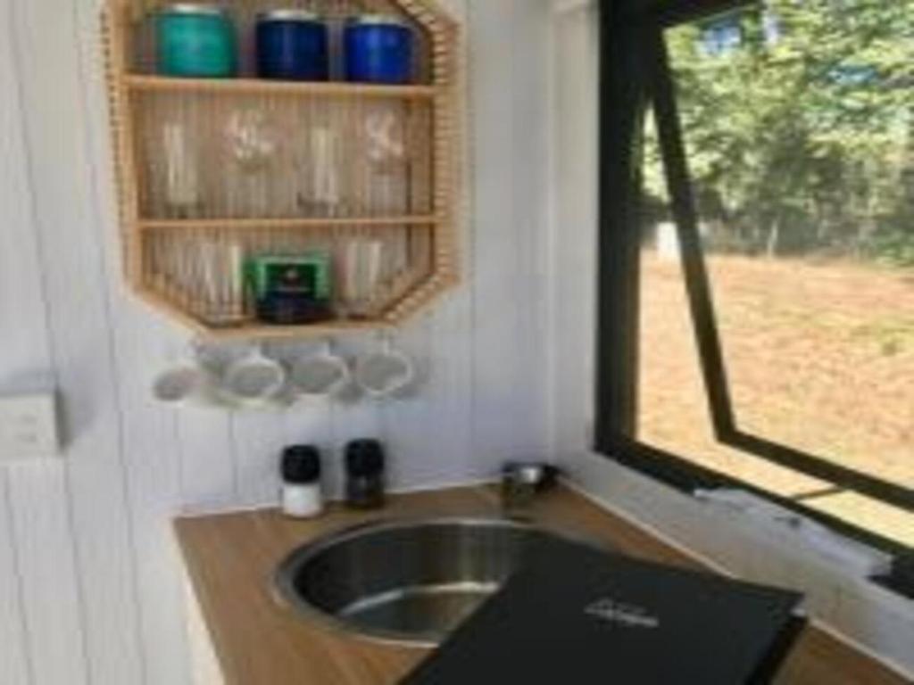 uma pequena cozinha com um lavatório e uma janela em White Jacaranda Tiny House em Maleny
