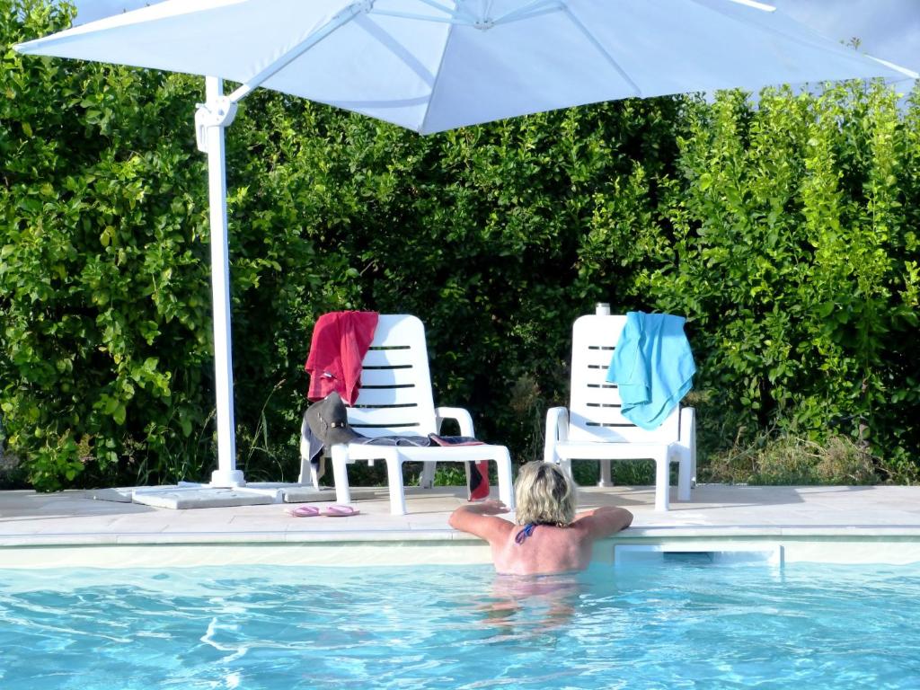 a person in a swimming pool next to two chairs and an umbrella at L'antico Trappeto Holiday Home in Noto