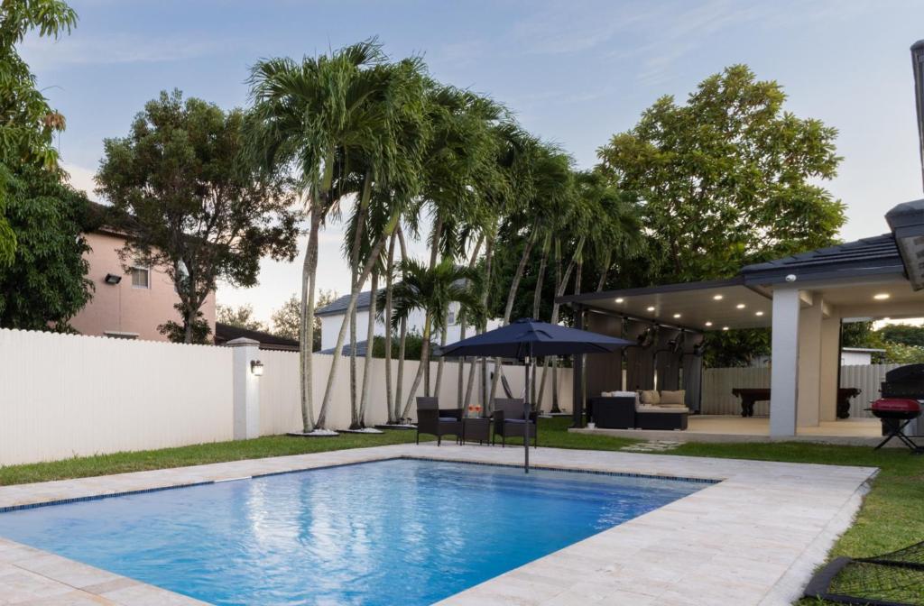 einen Pool mit Sonnenschirm und Palmen in der Unterkunft Miami Getaway Heated Pool Villa with Mini Golf &amp; BBQ in Miami