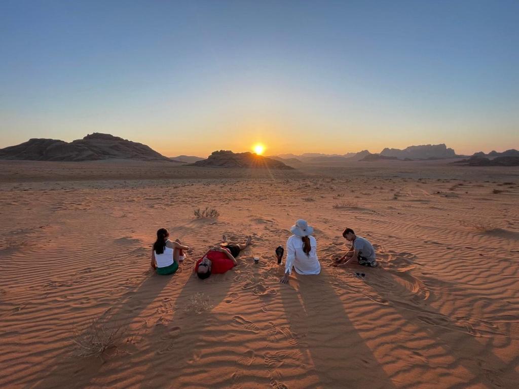 quatre personnes assises dans le désert regardant le coucher du soleil dans l'établissement Wadi Rum Classic Camp, à Wadi Rum