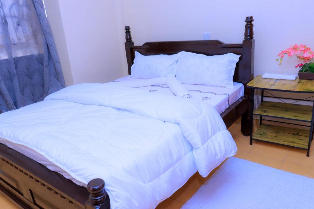 Schlafzimmer mit einem Bett mit weißer Bettwäsche und einem Tisch in der Unterkunft CALMCORNER HAVEN HOMES, PATRIDE ENTERPRISES in Kisii