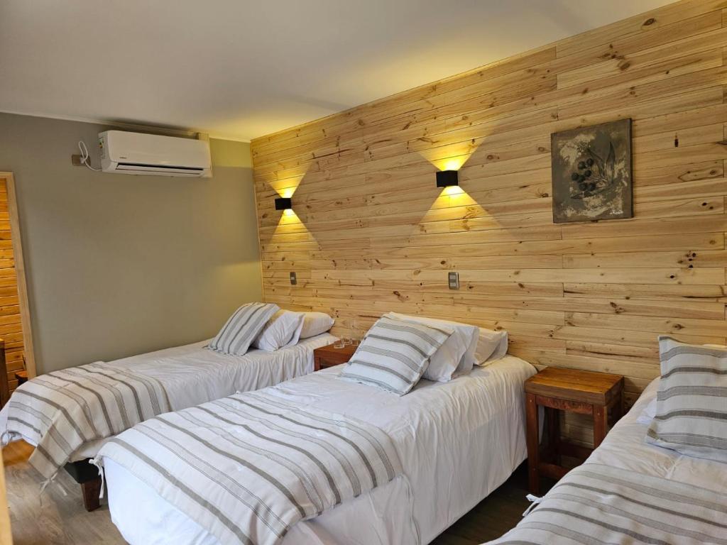 three beds in a room with wooden walls at Hotel Bacaris in Puerto Tranquilo