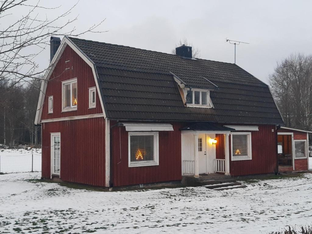 een rood huis met een zwart dak in de sneeuw bij Brofors in Forsheda